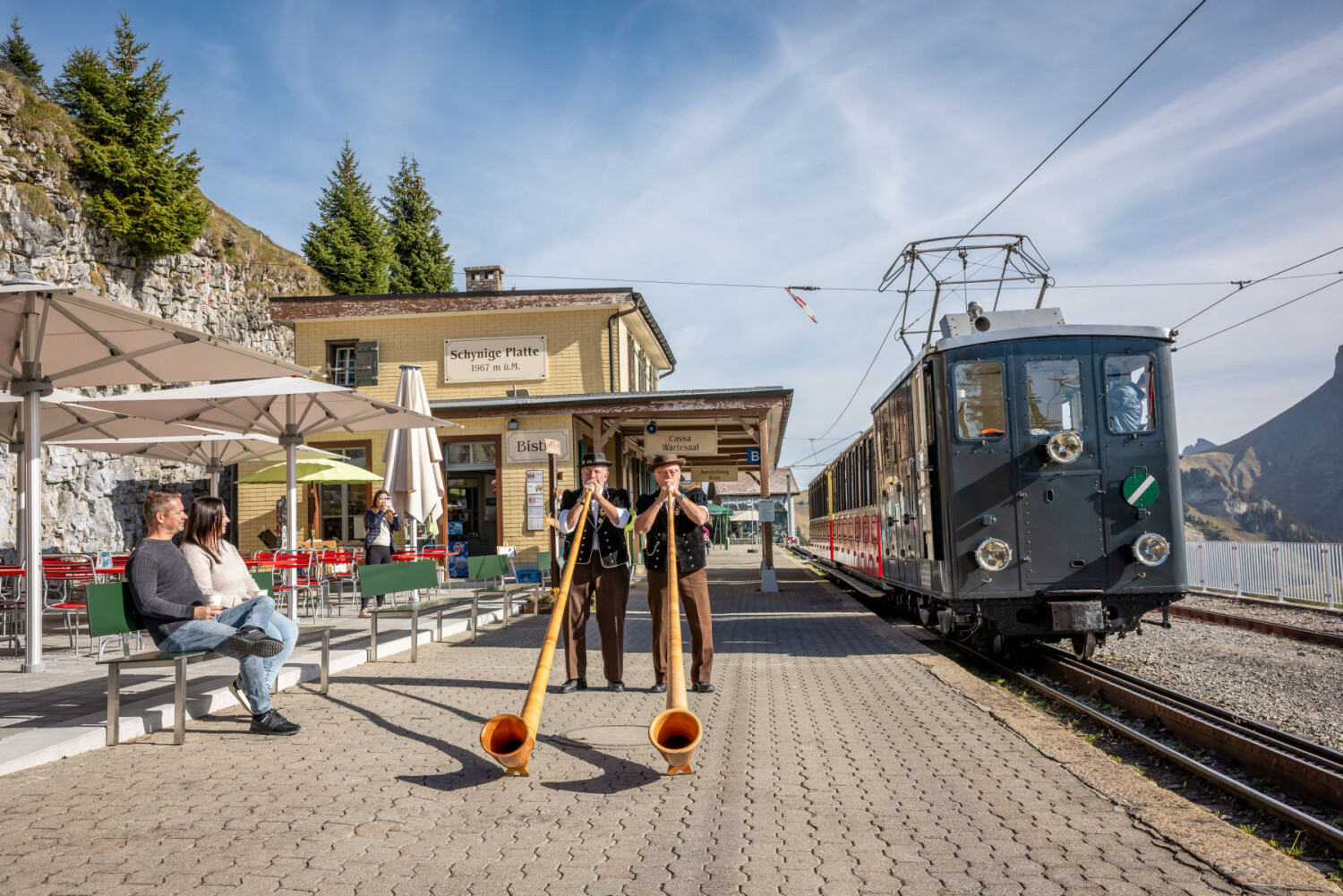 Schynige Platte Bahnhof Alphornblaeser zwei Personen auf Baenkli